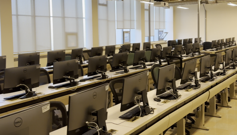 A photograph of rows computer setups, showing the back side of the monitors.